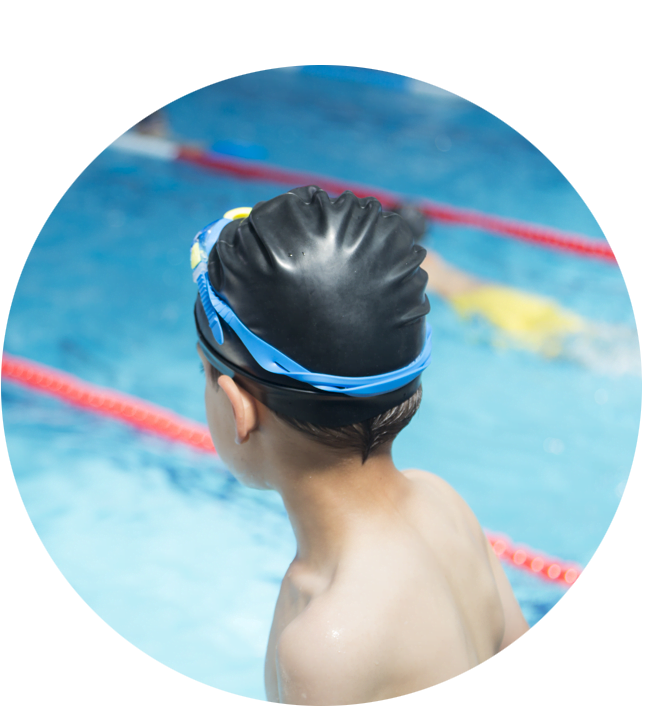 A close-up of a child wearing goggles and a swimming cap looking over a pool