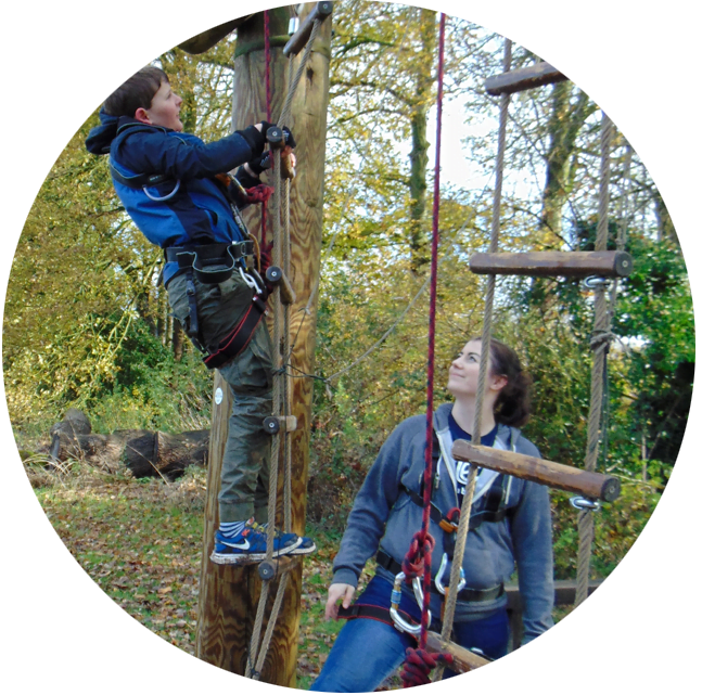 A Me2 Club member of staff watching a child doing an outdoor climbing activity.