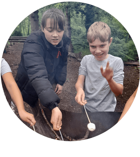 A child and volunteer toasting marshmallows over a fire pit