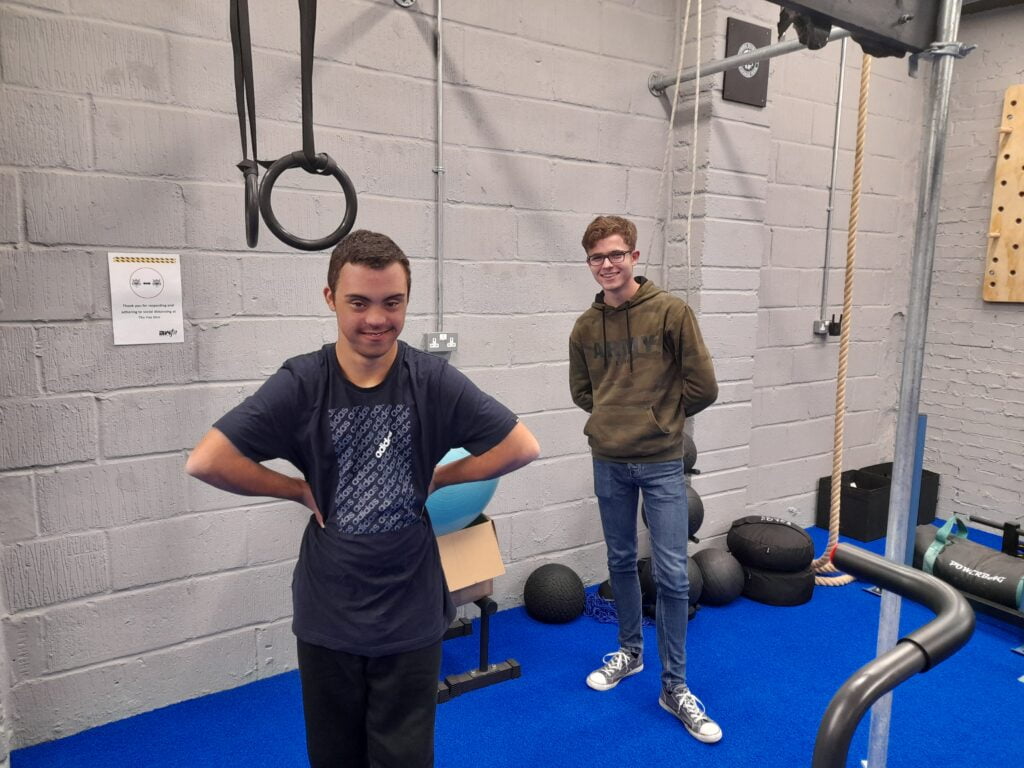 A teenager and volunteer standing in a gym and smiling for the camera